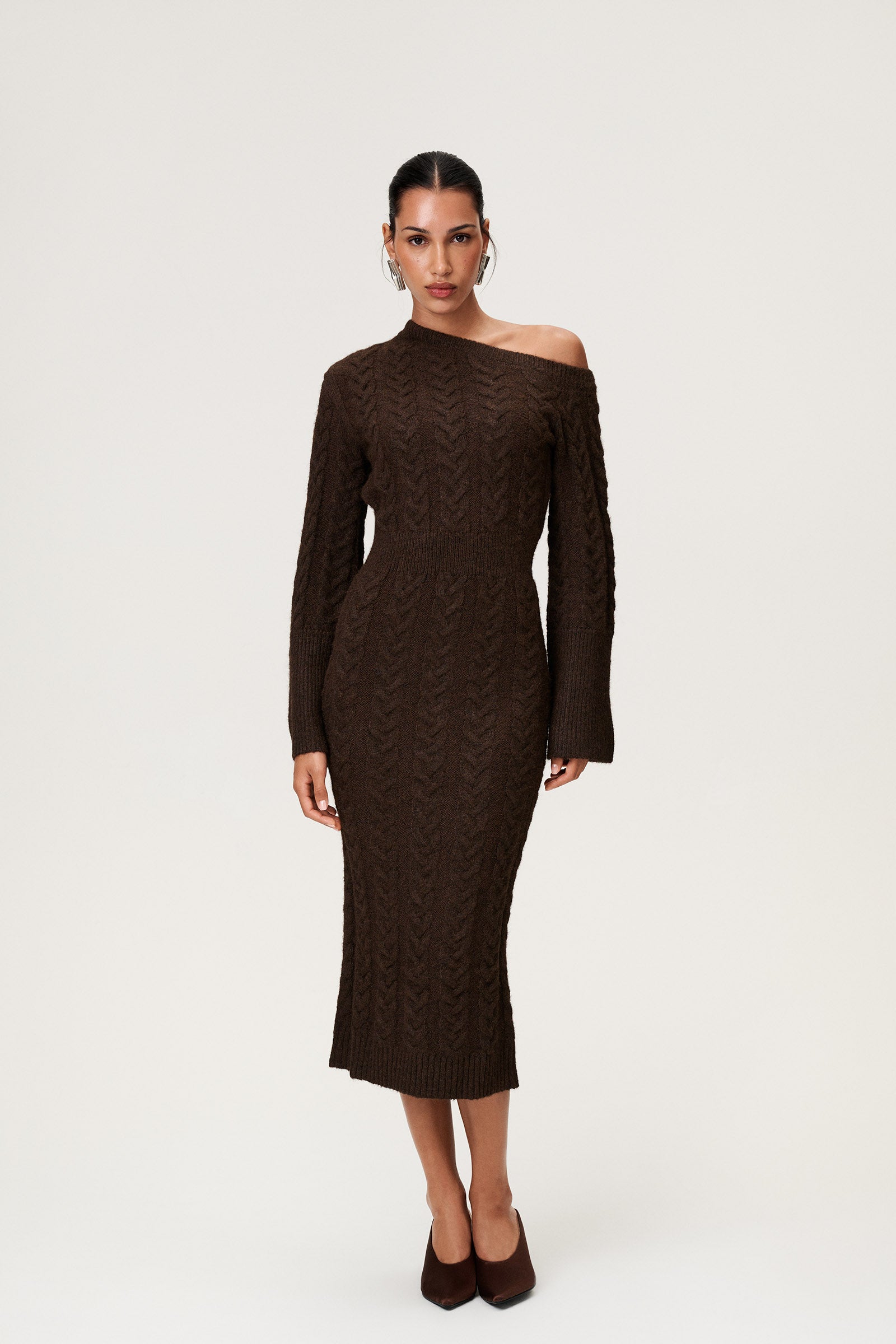Woman wearing the Arona knitted midi dress in brown melange with one padded shoulder, full-length sleeves, a back slit, and a heavy cable-knit design. image