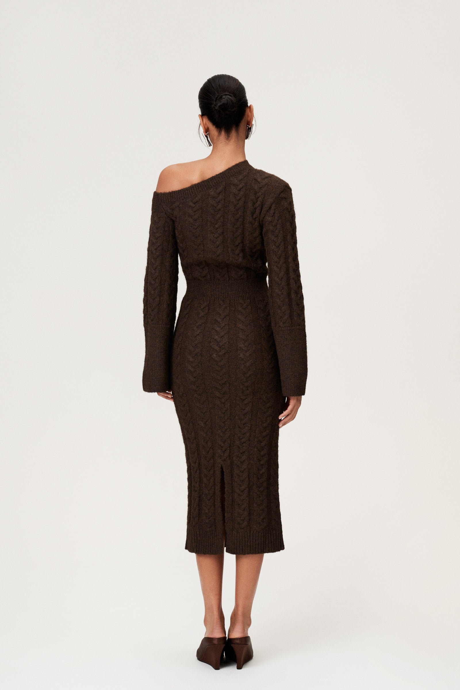 Woman wearing the Arona knitted midi dress in brown melange with one padded shoulder, full-length sleeves, a back slit, and a heavy cable-knit design. image