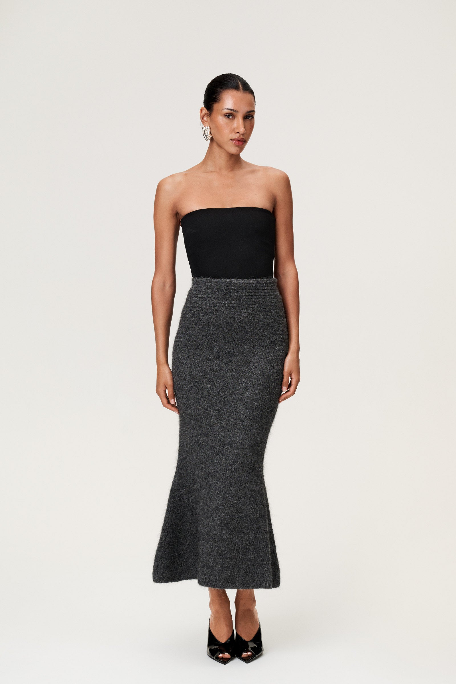 Woman wearing a Cessole midi skirt in dark grey. The skirt features a structured knit, midi length, zipper on the side, curved cutline in the waist, and softly flared bottom. image