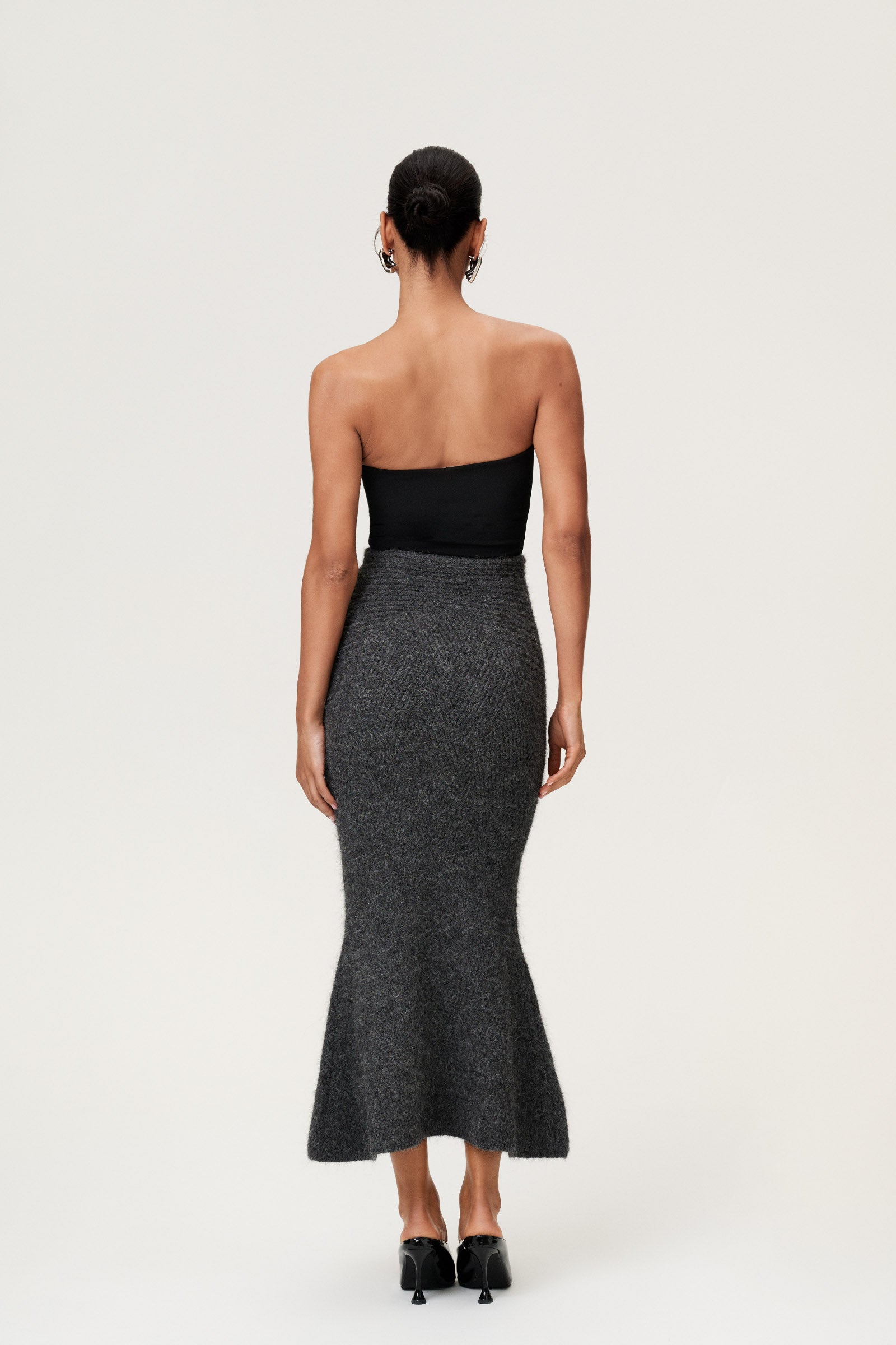 Woman wearing a Cessole midi skirt in dark grey. The skirt features a structured knit, midi length, zipper on the side, curved cutline in the waist, and softly flared bottom. image