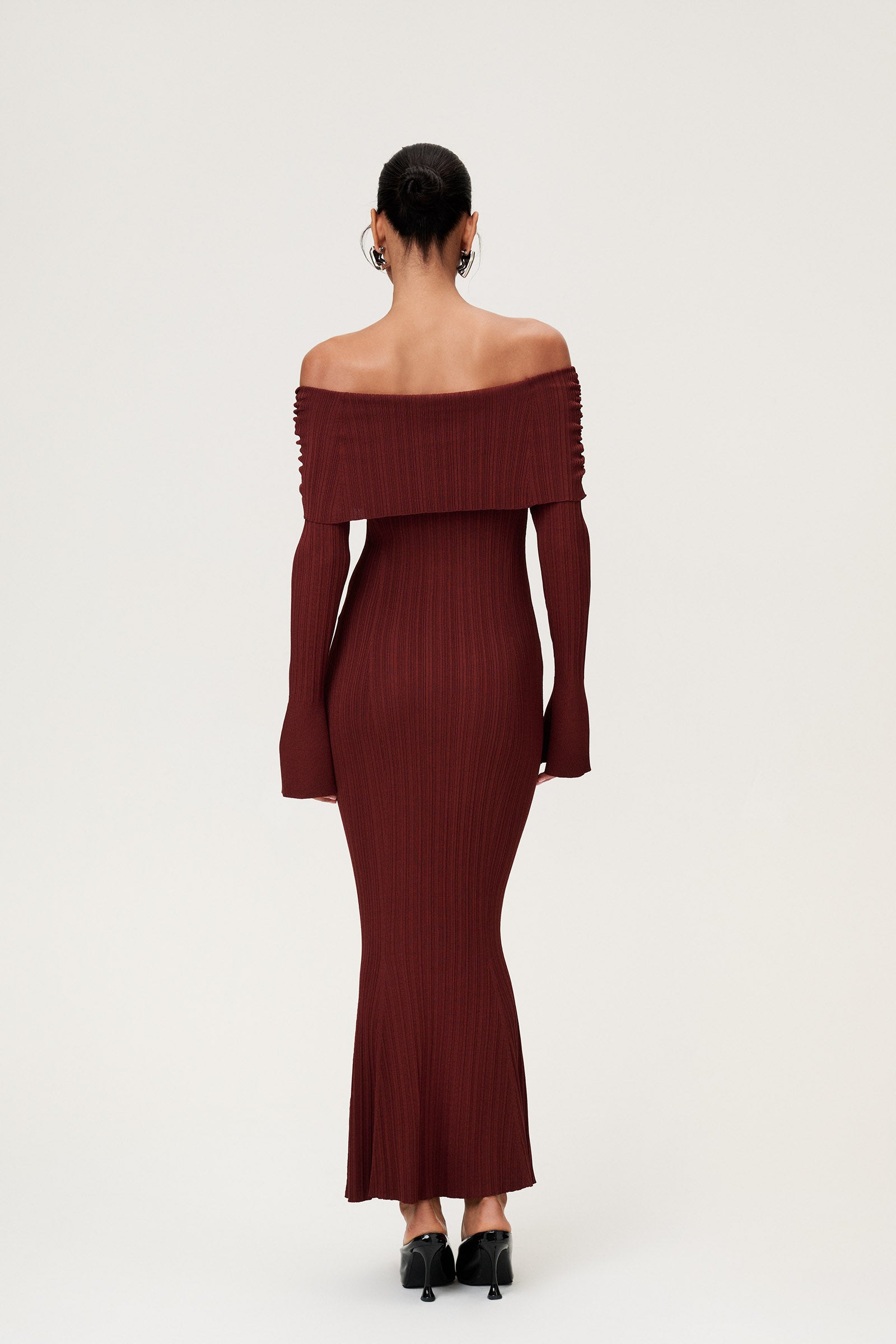 Woman wearing the Izano dress in burgundy, a knitted off-shoulder maxi dress with ruched panel detailing, soft draping, and a flowing, cozy silhouette. image