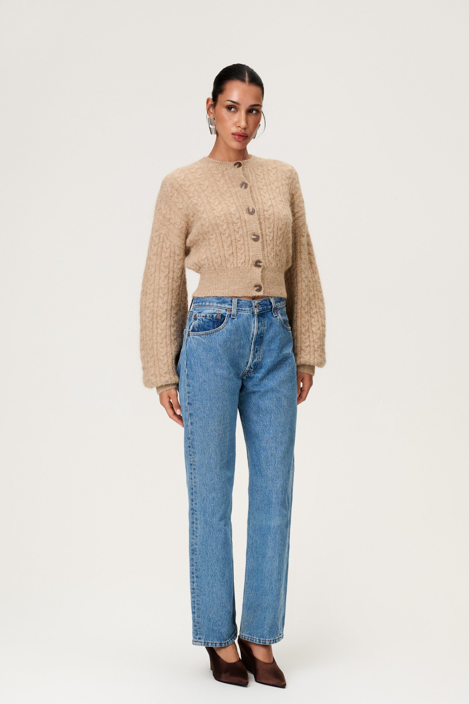 Woman wearing the Merano cardigan in beige melange, a cropped knit with puff sleeves, dropped shoulders, fitted cuffs, and a ribbed waist with button closure. image