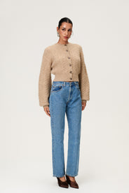 Woman wearing the Merano cardigan in beige melange, a cropped knit with puff sleeves, dropped shoulders, fitted cuffs, and a ribbed waist with button closure. thumbnail image