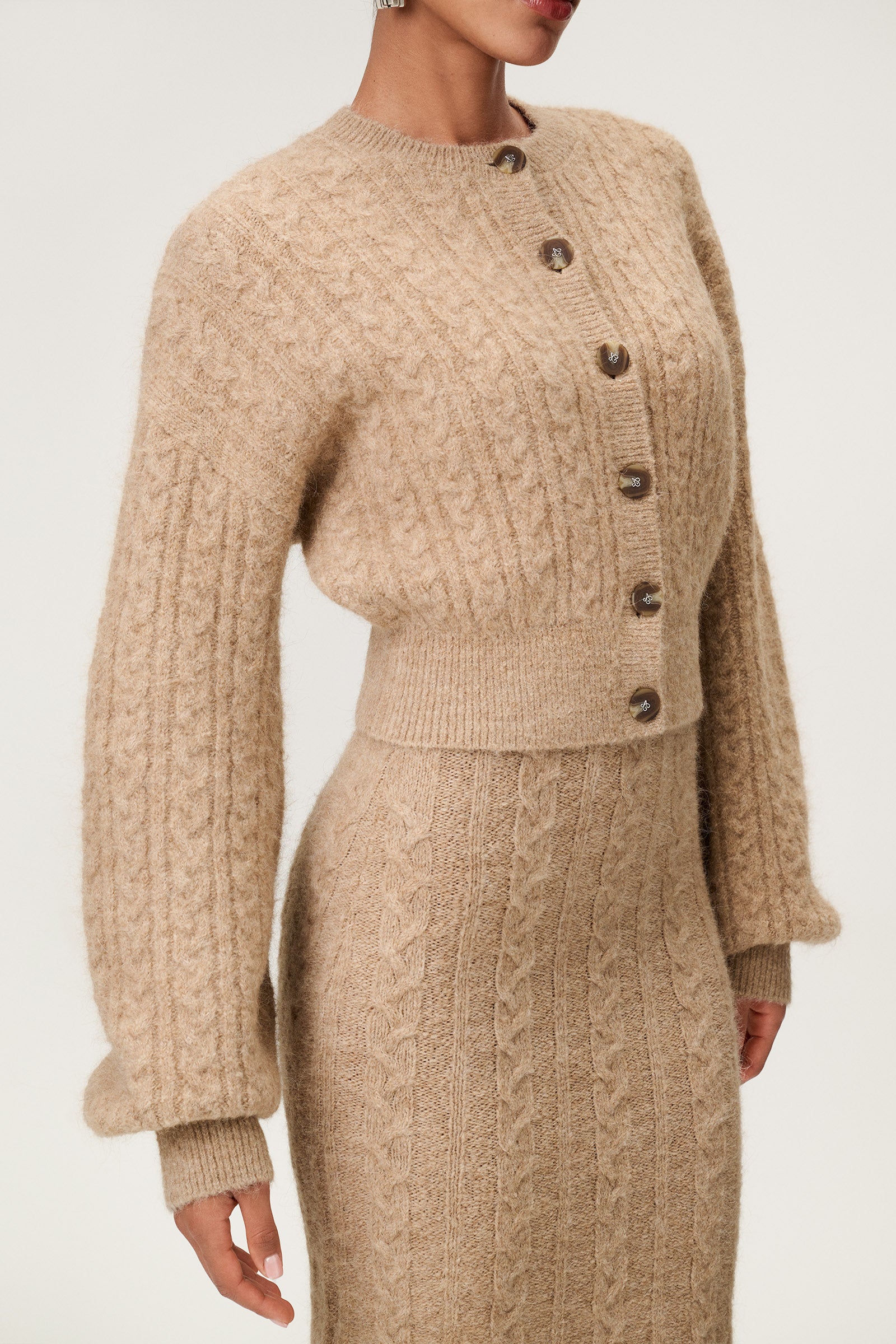 Woman wearing the Merano cardigan in beige melange, a cropped knit with puff sleeves, dropped shoulders, fitted cuffs, and a ribbed waist with button closure. image