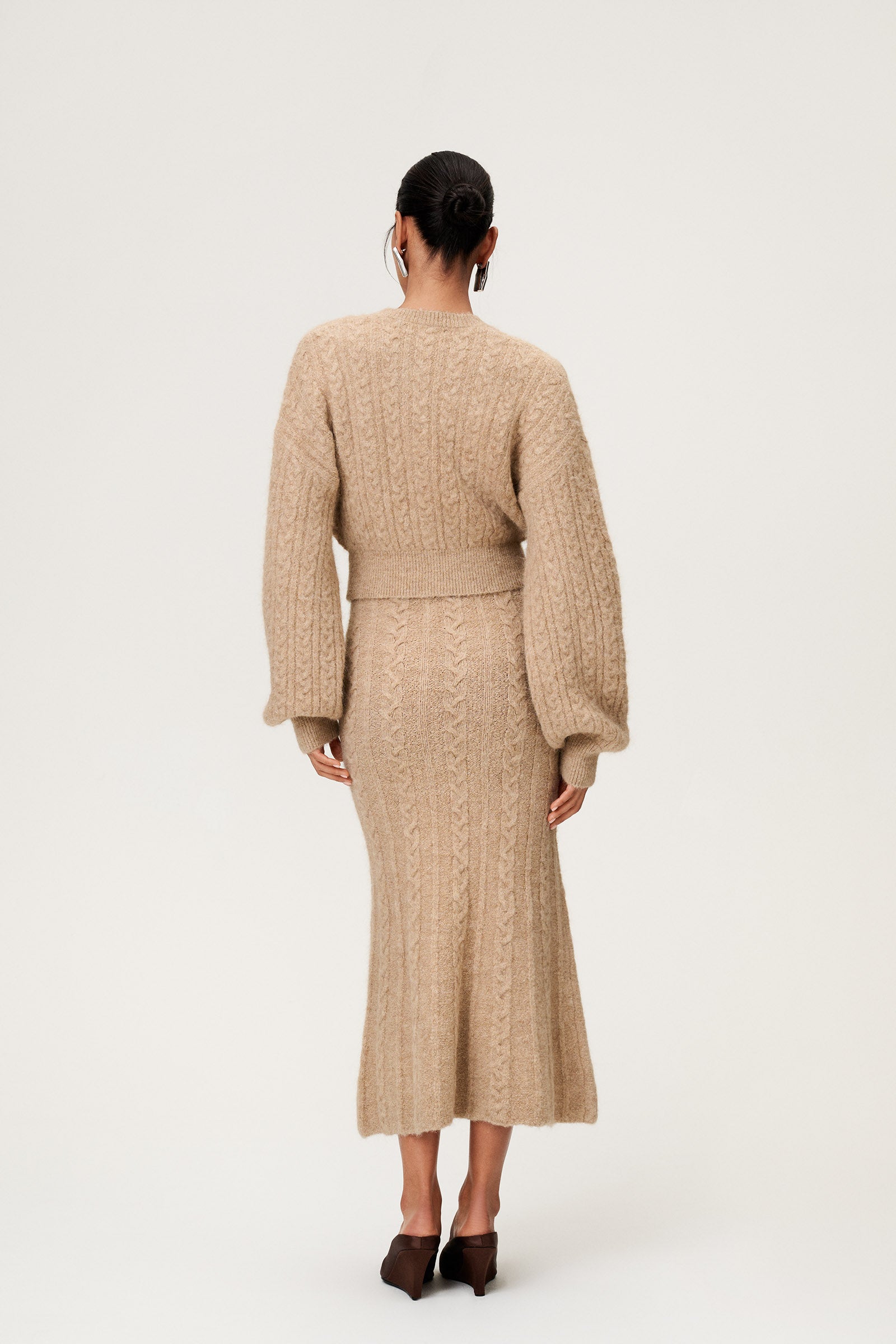 Woman wearing the Merano cardigan in beige melange, a cropped knit with puff sleeves, dropped shoulders, fitted cuffs, and a ribbed waist with button closure. image