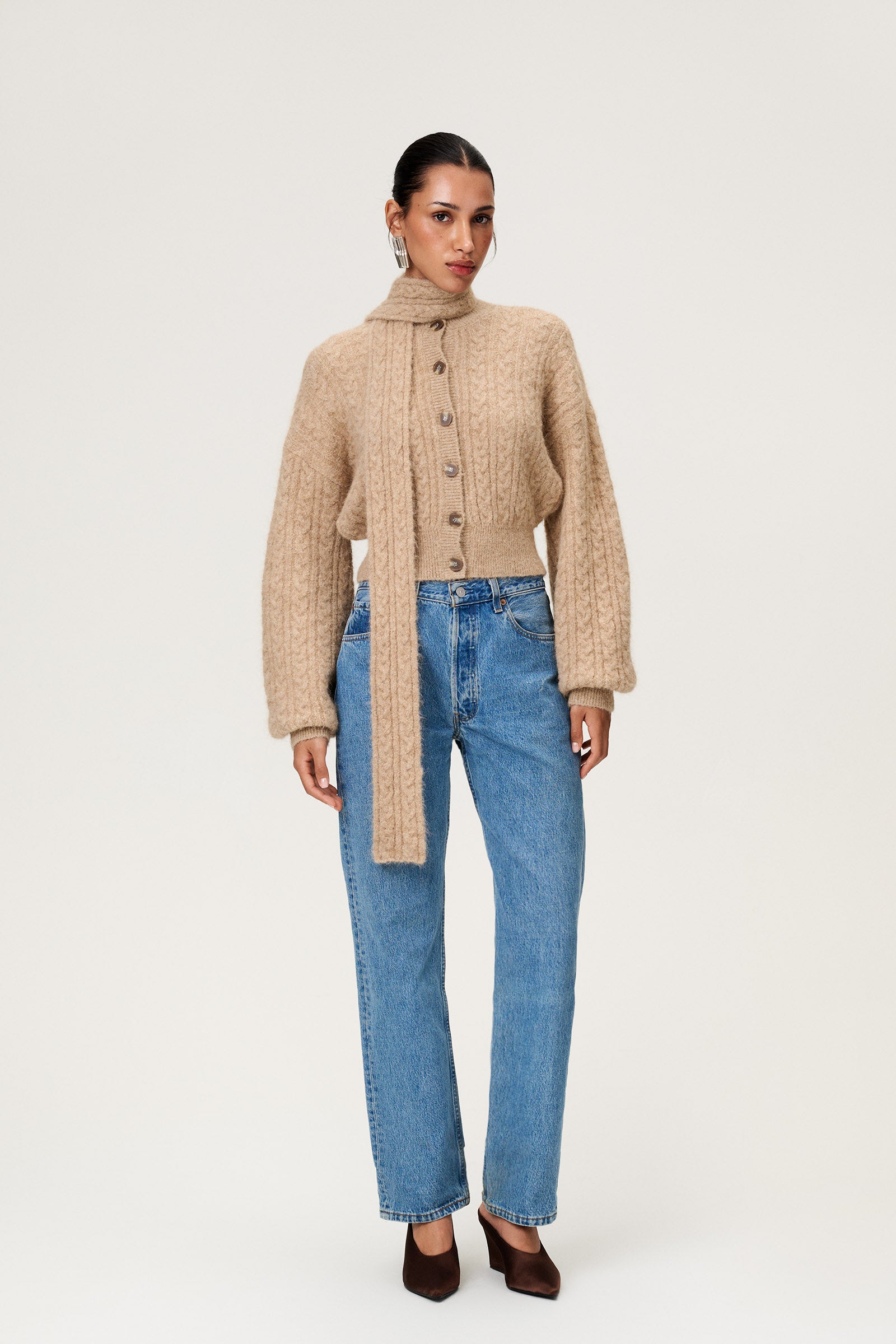 Woman wearing the Merano scarf styled with the Merano cardigan in beige melange, a cropped knit with puff sleeves, dropped shoulders, fitted cuffs, and a ribbed waist with button closure. image