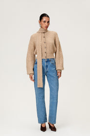 Woman wearing the Merano scarf styled with the Merano cardigan in beige melange, a cropped knit with puff sleeves, dropped shoulders, fitted cuffs, and a ribbed waist with button closure. thumbnail image