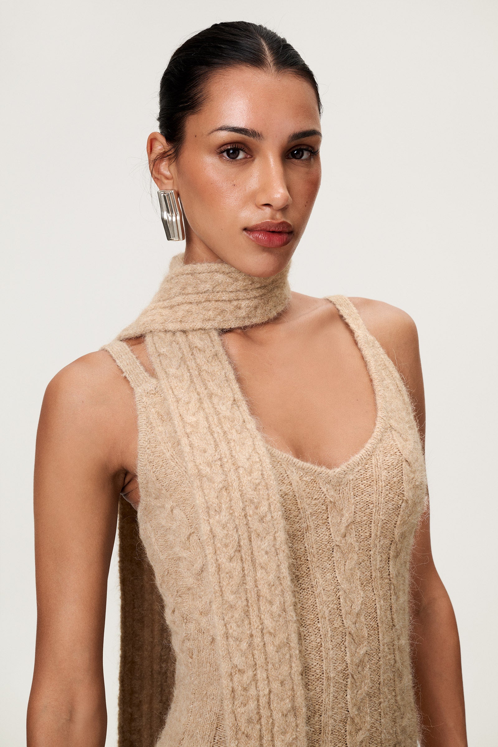 Woman wearing the Merano scarf in beige melange, styled with Merano dress in beige melange. The scarf is a lightweight knit with a soft texture, perfect for year-round layering. image