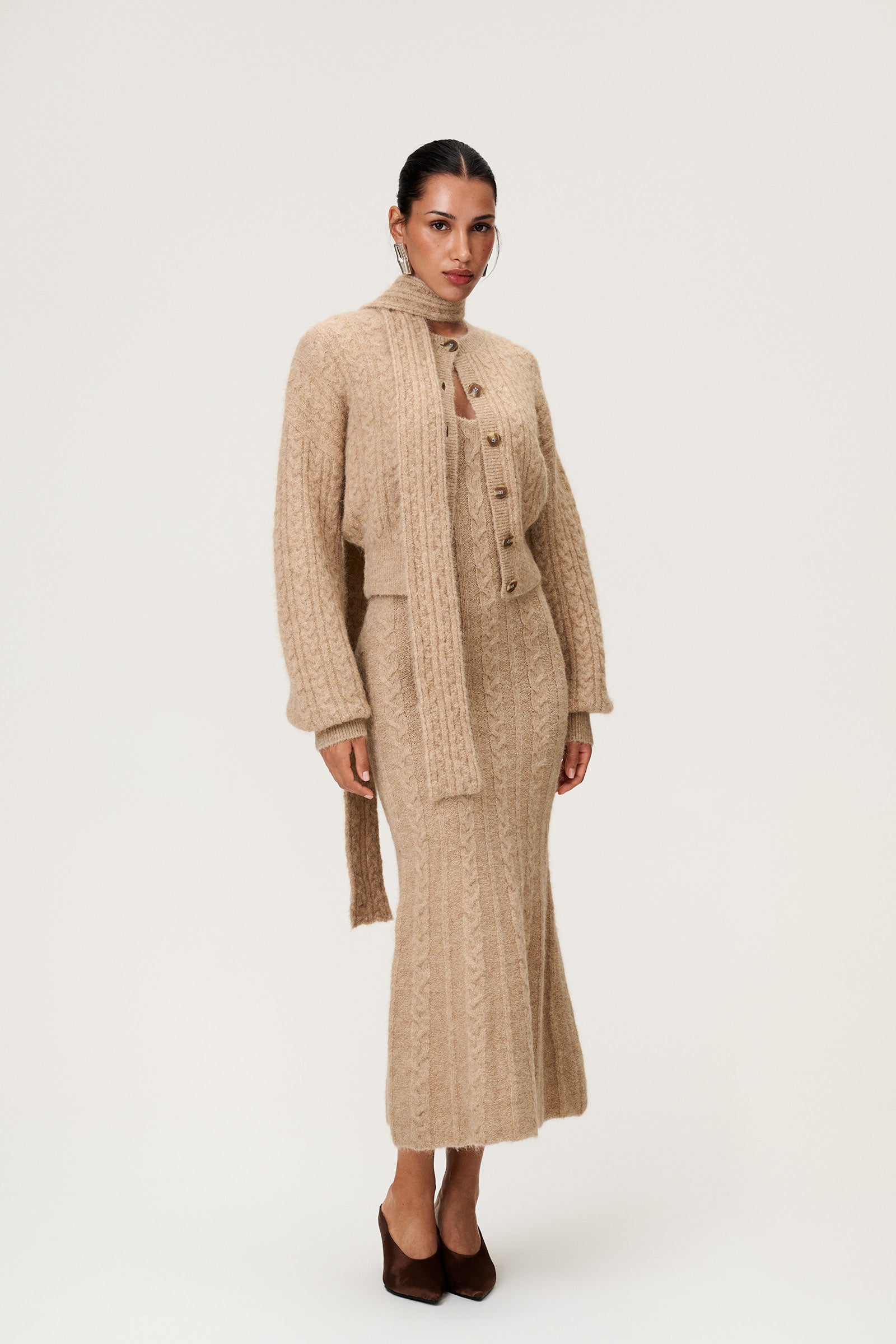 Woman wearing the Merano scarf in beige melange, styled with Merano dress and Merano cardigan in beige melange. The scarf is a lightweight knit with a soft texture, perfect for year-round layering. image