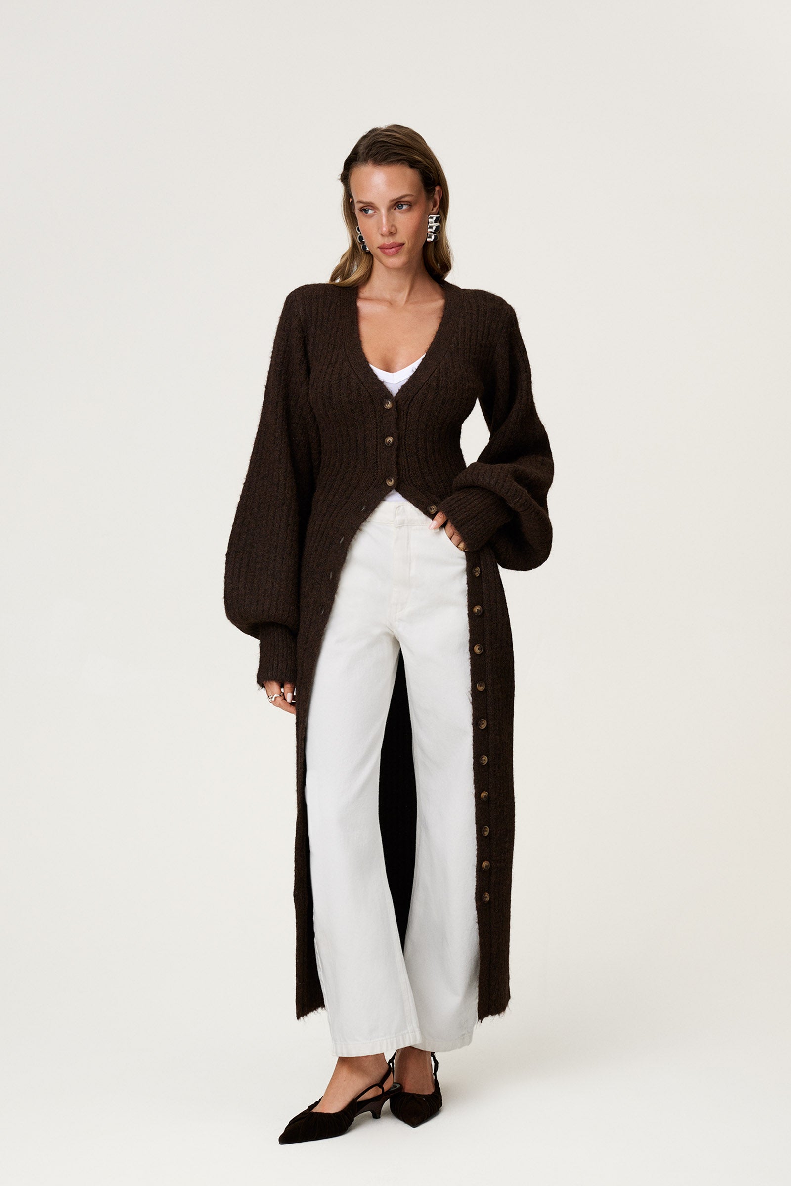 Woman wearing the Montana maxi dress in brown melange styled as a cardigan with jeans. The dress features an hourglass knit with a button-up front, V-neck collar, and balloon sleeves with cuff details. image