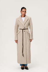 Woman wearing the Stockholm coat in beige melange. A full-length, hourglass coat with a cinched waist, removable suede belt, and structured shoulders. Finished with front pockets and a fully lined interior for warmth and comfort. thumbnail image